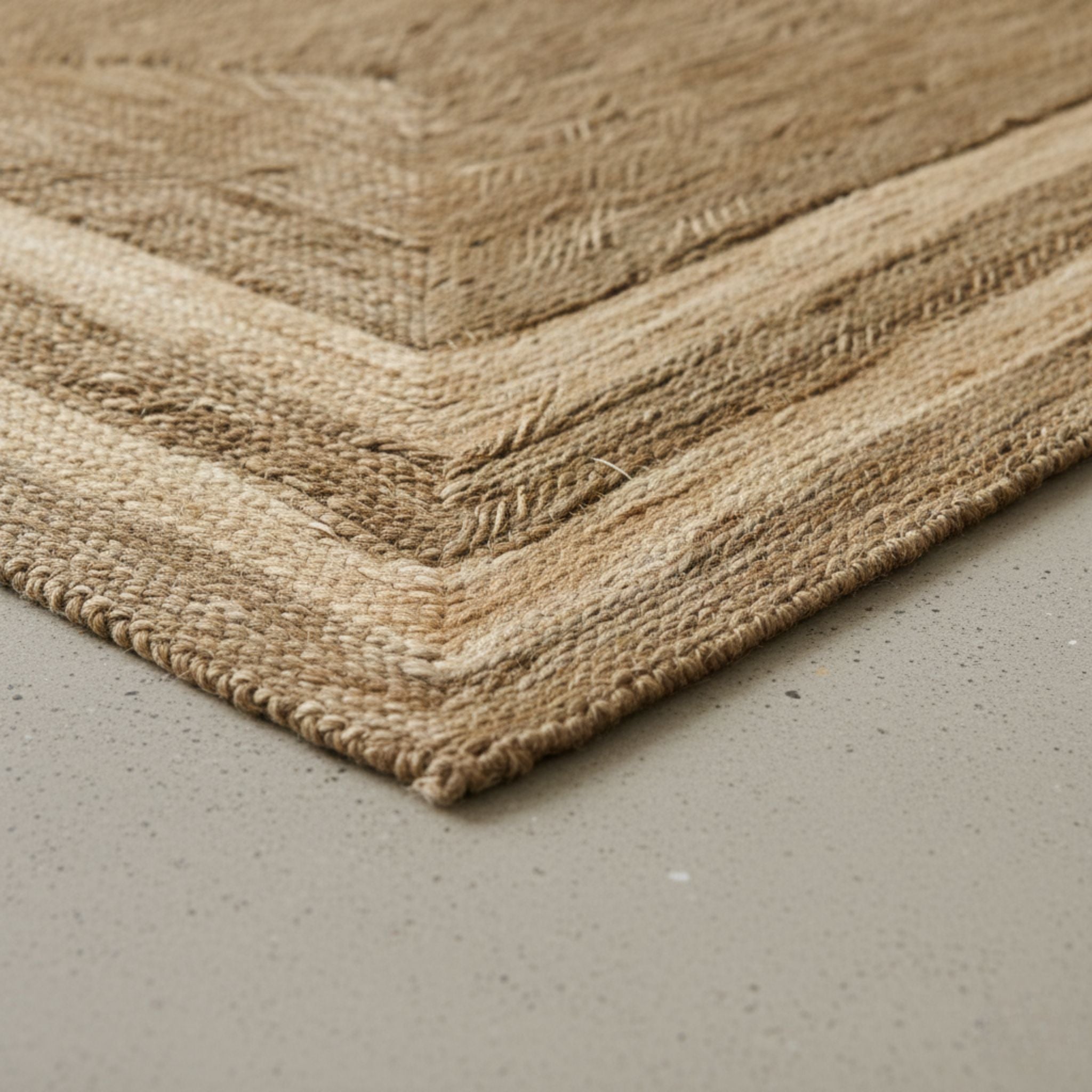 Detalle de primer plano del tapete Ulu que muestra el intrincado tejido de alga marina natural y la textura del borde escalonado sobre un piso de concreto minimalista.